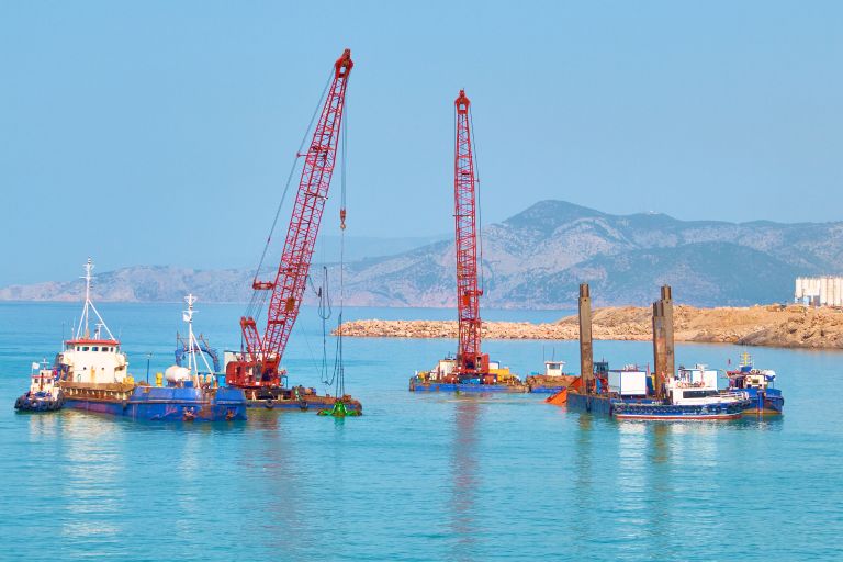 Commercial marine equipment including cranes and barges operating near shore in a working harbor