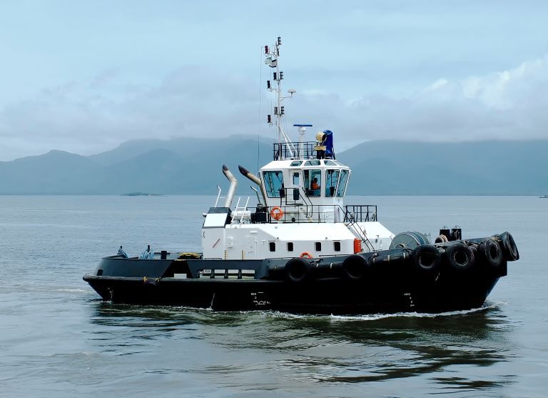 Black and white commercial tugboat cruising near mountains