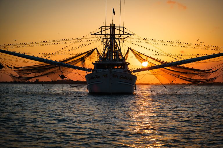 Shrimp trawler with extended nets at sunset on calm water