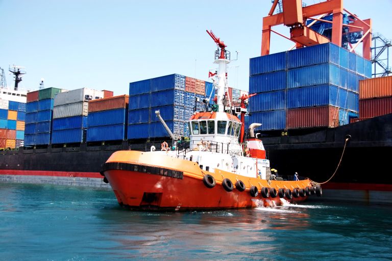 Bright orange commercial tugboat assisting cargo ship at a busy container port
